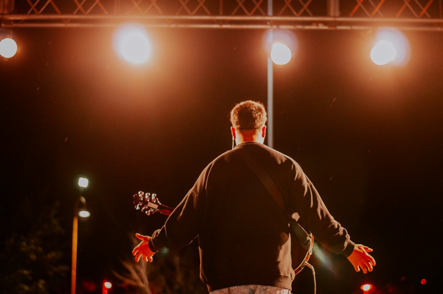Musician with outstretched arms holding guitar on stage at night.