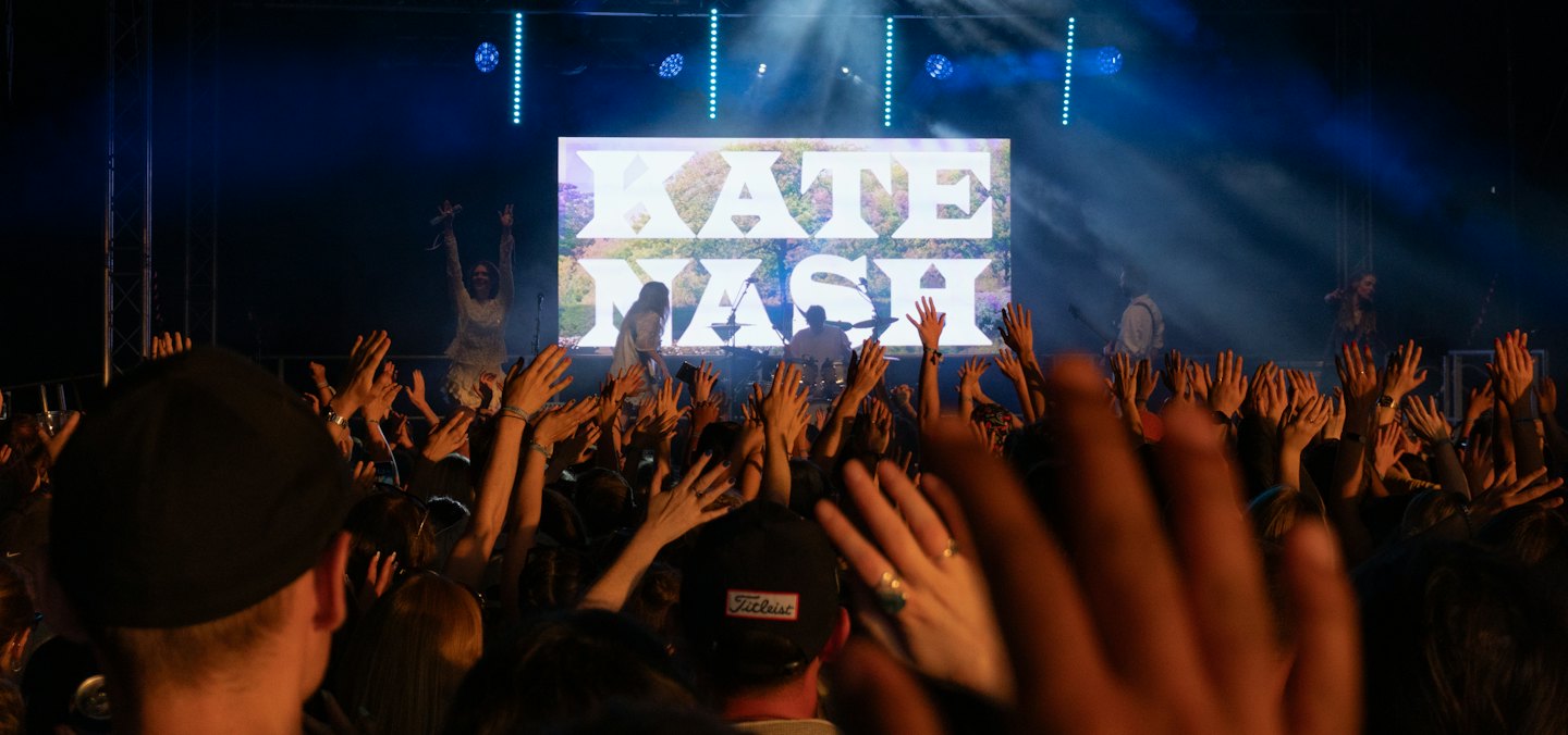 Concert audience reaching toward performers on a brightly lit stage.
