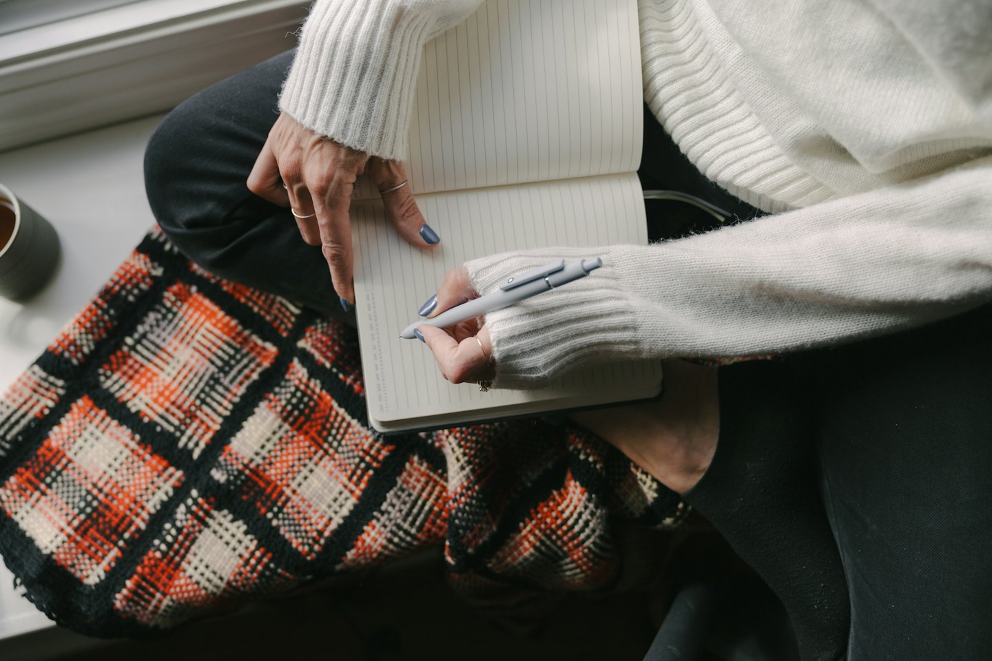 Person with blue nail polish writes in notebook with grey pen.